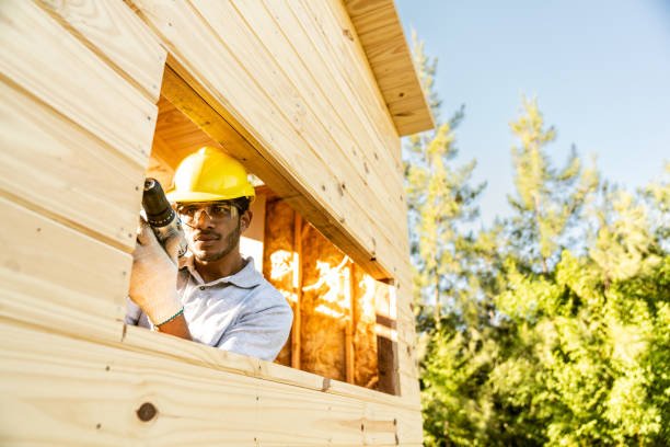 Construction worker uses electric screwdriver to prepare for window frame installation on wooden house