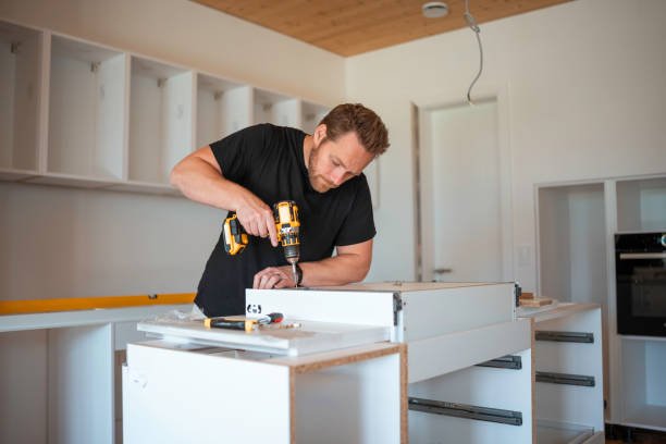 Focused mid adult Caucasian man uses a cordless drill to assemble a kitchen cabinet, demonstrating skill in home improvement and interior design.